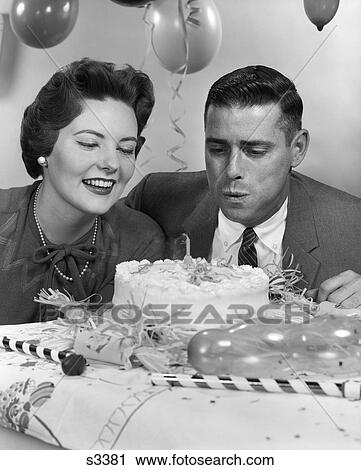Stock Image - 1950S 1960S Couple With Birthday Cake Man Blowing Out Candle . Fotosearch