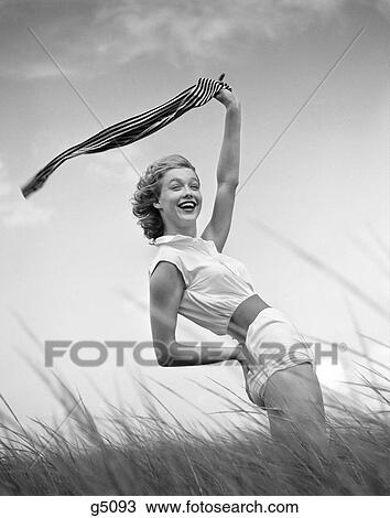 1950S 1960S Woman In White Shorts & Blouse Bending Back Holding A Scarf Up Into The Wind Standing On Grassy Beach Dune View Large Photo Image Stock Image - 1950S 1960S Woman In White Shorts & Blouse Bending Back Holding A Scarf Up Into The Wind Standing On Grassy Beach Dune . Fotosearch