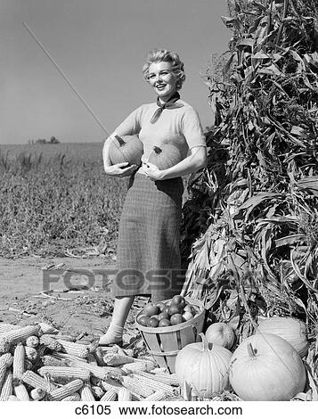 1950S 1960S Woman Standing By Corn Shock Holding A Pumpkin Under Each Arm View Large Photo Image Stock Photography - 1950S 1960S Woman Standing By Corn Shock Holding A Pumpkin Under Each Arm . Fotosearch