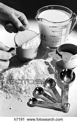 Stock Image - 1950S 1960S Woman’S Hand Leveling Off Flour In Measuring Cup For Baking. Fotosearch