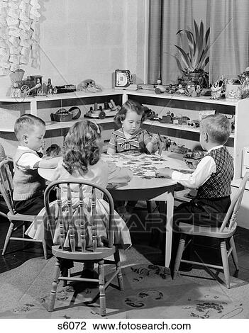 Stock Image - 1950S 4 Dressed-Up School Children Seated At Small Round Table Putting Together Jigsaw Puzzle . Fotosearch
