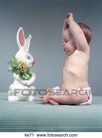 1950S Baby Full Figure Seated Arms Above Head Looking At Easter Rabbit Toy Green Bow Flowers Diaper Blue Background View Large Photo Image Stock Image - 1950S Baby Full Figure Seated Arms Above Head Looking At Easter Rabbit Toy Green Bow Flowers Diaper Blue Background. Fotosearch