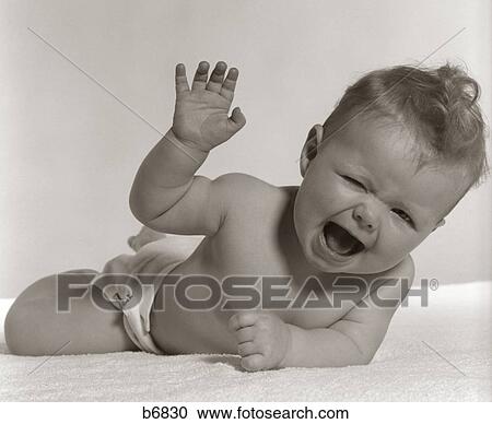 Stock Image - 1950S Baby Lying On Stomach Laughing With Squinted Eyes & Hand In Air . Fotosearch