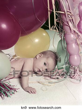 Stock Photo - 1950S Baby Lying On White Blanket Amid Pink Yellow Red New Year Balloons And Streamers Party Celebration. Fotosearch