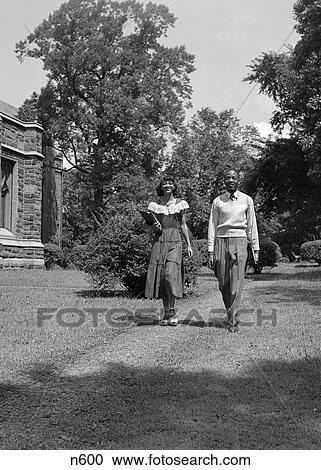1950S Black College Age Couple Walking On Lawn Through Campus Carrying Books View Large Photo Image Stock Image - 1950S Black College Age Couple Walking On Lawn Through Campus Carrying Books . Fotosearch