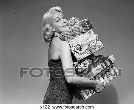 Stock Image - 1950S Blonde Woman Strapless Dress Carrying Stack Gift Wrapped Presents Christmas Packages . Fotosearch