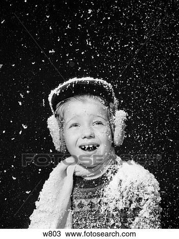 Stock Image - 1950S Boy Catching Snowflakes In Open Mouth Snow Falling Ear Muffs Hat Scarf In Studio . Fotosearch