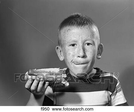 Stock Image - 1950S Boy With Freckles Short Haircut Licking His Lips & Holding A Hot Dog With A Bite Taken Out Of It. Fotosearch