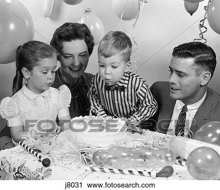 Stock Image - 1950S Close-Up Of Family Of 4 With Son Blowing Out 2 Candles On His Birthday Cake . Fotosearch