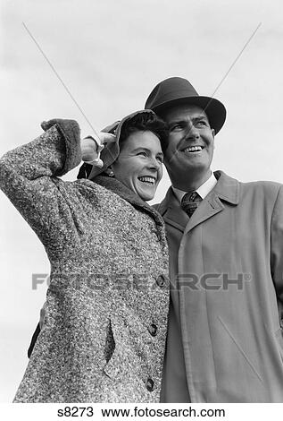 1950S Couple In Coats & Hats With Arms Around Each Other Looking Off Into Distance View Large Photo Image Stock Image - 1950S Couple In Coats & Hats With Arms Around Each Other Looking Off Into Distance . Fotosearch