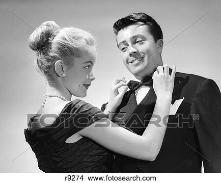 1950S Couple In Formal Attire Woman With Blonde Hair Pulled Back In Bun Adjusting Man'S Bow Tie Smiling Perky Cute View Large Photo Image Picture - 1950S Couple In Formal Attire Woman With Blonde Hair Pulled Back In Bun Adjusting Man'S Bow Tie Smiling Perky Cute. Fotosearch