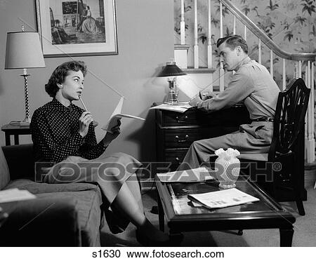 1950S Couple In Living Room Look Over Household Bills Finance Woman On Couch List In Hand Man Sits At Desk By Stairs View Large Photo Image Stock Image - 1950S Couple In Living Room Look Over Household Bills Finance Woman On Couch List In Hand Man Sits At Desk By Stairs. Fotosearch