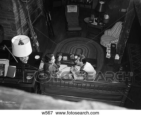 Stock Photo - 1950S Couple Man Woman Sit Couch Ski Lodge Lamp Chair Skiis Brick Wall Rug Shot From Above . Fotosearch