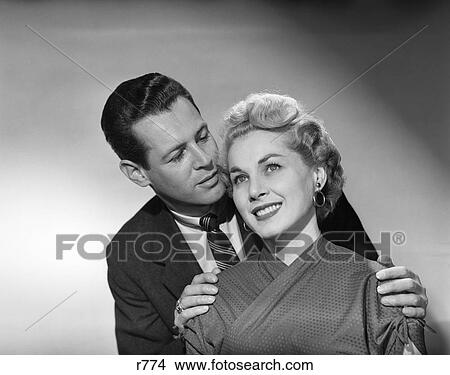 1950S Couple Portrait Smiling Man Behind Woman Whisper In Ear Hands On Her Shoulders View Large Photo Image Picture - 1950S Couple Portrait Smiling Man Behind Woman Whisper In Ear Hands On Her Shoulders . Fotosearch