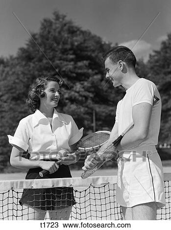 1950S Couple Standing On Opposite Sides Of Net Holding Raquets & Ball & Talking View Large Photo Image Stock Image - 1950S Couple Standing On Opposite Sides Of Net Holding Raquets & Ball & Talking . Fotosearch