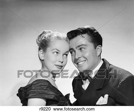 Stock Image - 1950S Cute Couple Man Woman Foreheads Touching Look Into Each Others Eyes Formal Dress Pearls Tuxedo Silly Expression. Fotosearch
