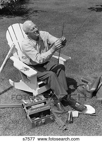 1950S Elderly Man In Backyard Seated In Wooden Chair Threading Line Through Fishing Rod With Boots & Tackle Box At Feet View Large Photo Image Stock Photo - 1950S Elderly Man In Backyard Seated In Wooden Chair Threading Line Through Fishing Rod With Boots & Tackle Box At Feet. Fotosearch