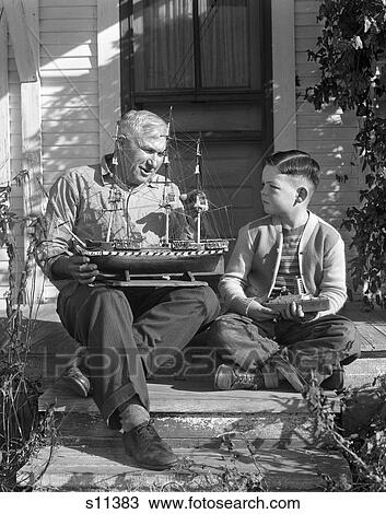 1950S Elderly Man Talking To A Young Boy As Both Are Sitting On The Steps Holding Model Ships Man Of War Backdoor View Large Photo Image Stock Image - 1950S Elderly Man Talking To A Young Boy As Both Are Sitting On The Steps Holding Model Ships Man Of War Backdoor . Fotosearch