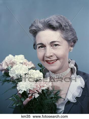 Stock Photography - 1950S Elderly Senior Woman Portrait Gray Hair Smiling Smile Holding Bouquet Of Pink White Carnations Grandmother Mom. Fotosearch