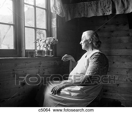 1950S Elderly Woman Seated In Dimly Lit Farmhouse With Plants On Windowsill Looking Out Window With Sunlight Shining Through View Large Photo Image Picture - 1950S Elderly Woman Seated In Dimly Lit Farmhouse With Plants On Windowsill Looking Out Window With Sunlight Shining Through. Fotosearch