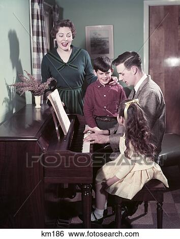 Stock Photograph - 1950S Family 4 Man Father Play Piano Mother Woman Boy Girl Son Daughter Sing Living Room Upright Vase Bench. Fotosearch