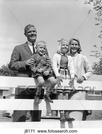 Stock Image - 1950S Family Of Four Behind Backyard Fence Smiling Towards Camera . Fotosearch