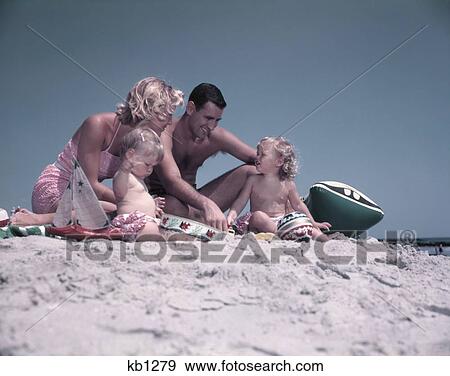 1950S Family Sitting On Sandy Beach Man Woman Mother Father Two Children Boy Girl Playing Sand Toys Summer Vacation View Large Photo Image Stock Photo - 1950S Family Sitting On Sandy Beach Man Woman Mother Father Two Children Boy Girl Playing Sand Toys Summer Vacation . Fotosearch