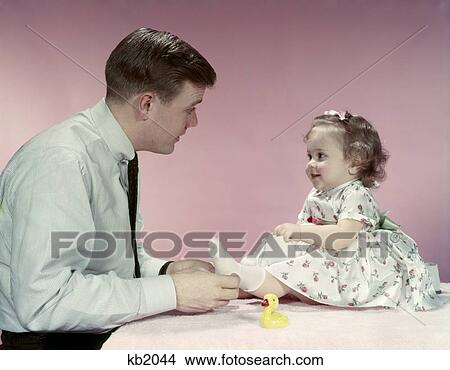 1950S Father Man Putting Socks On Little Baby Girl In Print Flowered Dress Pink And White Parent Daughter Dressing View Large Photo Image Picture - 1950S Father Man Putting Socks On Little Baby Girl In Print Flowered Dress Pink And White Parent Daughter Dressing. Fotosearch