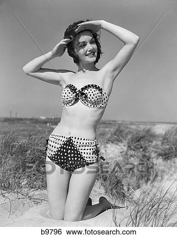 1950S Female Kneeling In Grassy Sand Wearing Polka Dot Bikini Shading Eyes From Sun View Large Photo Image Stock Photograph - 1950S Female Kneeling In Grassy Sand Wearing Polka Dot Bikini Shading Eyes From Sun . Fotosearch