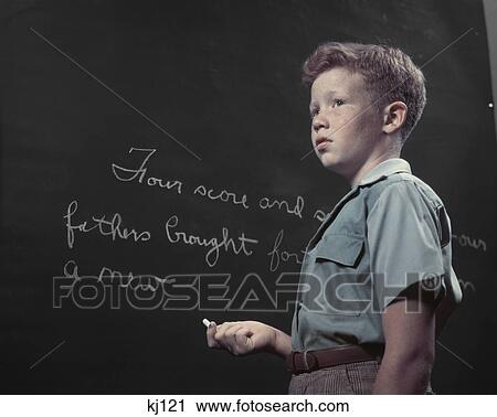 Stock Image - 1950S Freckle Faced Red Haired Boy At Blackboard Writing With Chalk Gettysburg Address School History Class Four Score. Fotosearch
