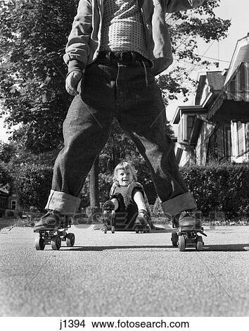 1950S Girl Fallen Sitting Sidewalk Wear Metal Roller Skates Shot Thru Legs Of Little Boy Rolled Cuff Blue Jeans View Large Photo Image Picture - 1950S Girl Fallen Sitting Sidewalk Wear Metal Roller Skates Shot Thru Legs Of Little Boy Rolled Cuff Blue Jeans . Fotosearch