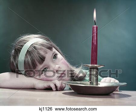 Stock Photograph - 1950S Girl Wistful Sad Thoughtful Lean Head On Arm On Table Look At Burning Red Candle In Brass Holder Make A Wish. Fotosearch