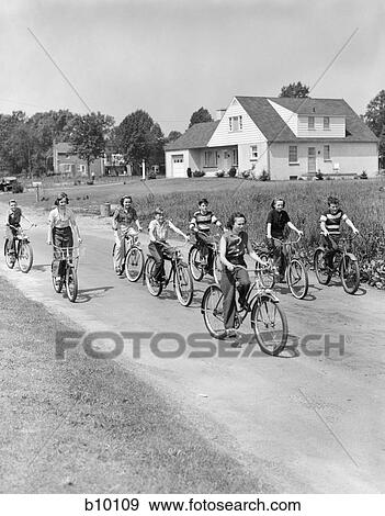 Stock Photo - 1950S Group Of 8 Kids Boys & Girls Ride Bicycles On Country Rural Road Lane Fun House In Background . Fotosearch