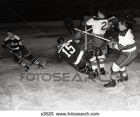 Stock Image - 1950S Hockey Game With One Of 4 Players In Foreground Being Knocked Down By 2 Opposing Team Members . Fotosearch