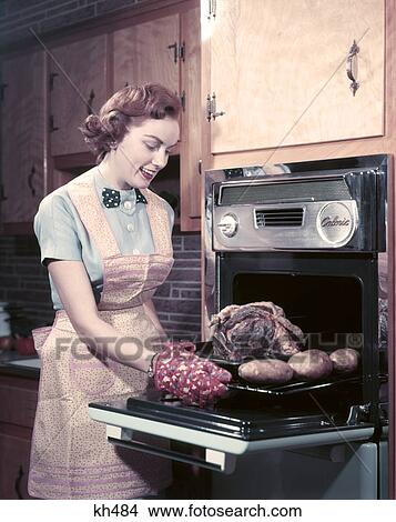 1950S Housewife Smiling Wear Apron Take Roast With Potatoes Out Of Oven Kitchen Cooking Oven Mitts Food Preparation Cook View Large Photo Image Picture - 1950S Housewife Smiling Wear Apron Take Roast With Potatoes Out Of Oven Kitchen Cooking Oven Mitts Food Preparation Cook. Fotosearch