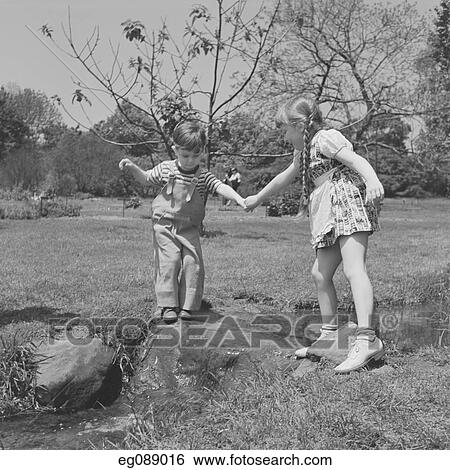 Stock Photograph - 1950S Little Girl Helping Younger Boy Across Stream . Fotosearch