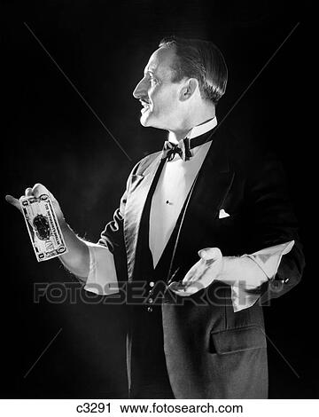 Stock Image - 1950S Magician In Tuxedo With Sleeves Rolled Up Holding Out Dollar Bill . Fotosearch