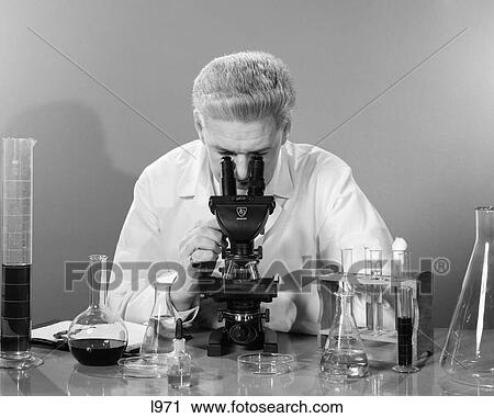 1950S Man In Lab Coat Sitting At Table Looking Through Microscope With Various Beakers Test Tubes & Petri Dishes View Large Photo Image Stock Image - 1950S Man In Lab Coat Sitting At Table Looking Through Microscope With Various Beakers Test Tubes & Petri Dishes . Fotosearch