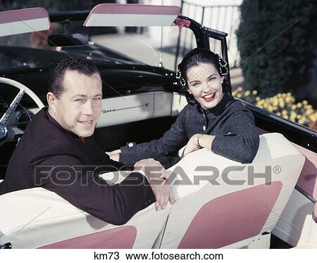 1950S Smiling Couple Man Woman In Front Seat Turned Look Back Convertible Pink & White Upholstery View Large Photo Image Stock Image - 1950S Smiling Couple Man Woman In Front Seat Turned Look Back Convertible Pink & White Upholstery . Fotosearch