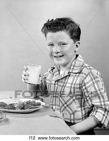 Stock Image - 1950S Smiling Freckle-Faced Boy Sitting At Dinner Table With Glass Of Milk In Hand . Fotosearch