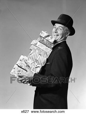 1950S Smiling Man Black Hat Carrying Stack Of Gift Wrapped Christmas Presents View Large Photo Image Stock Photo - 1950S Smiling Man Black Hat Carrying Stack Of Gift Wrapped Christmas Presents . Fotosearch