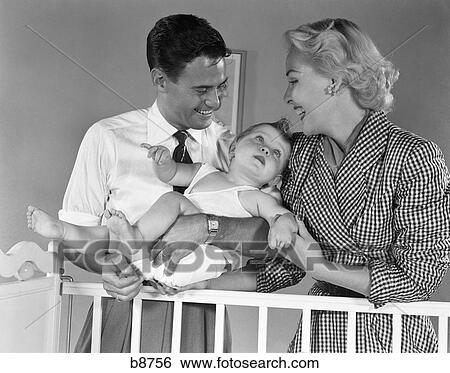 1950S Smiling Parents Picking Baby Up Out Of Crib View Large Photo Image Stock Photograph - 1950S Smiling Parents Picking Baby Up Out Of Crib . Fotosearch