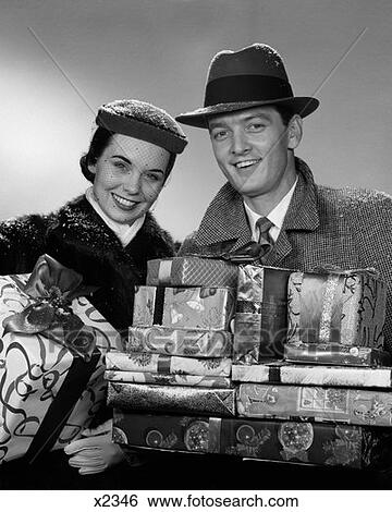 1950S Smiling Portrait Couple In Winter Coats & Hats Holding Wrapped Gifts View Large Photo Image Stock Photograph - 1950S Smiling Portrait Couple In Winter Coats & Hats Holding Wrapped Gifts . Fotosearch