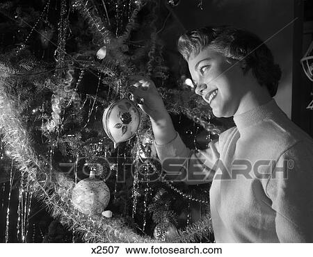 1950S Smiling Pretty Young Woman Hanging Glass Christmas Ornament On Branch Light Comes From The Tree View Large Photo Image Stock Photo - 1950S Smiling Pretty Young Woman Hanging Glass Christmas Ornament On Branch Light Comes From The Tree . Fotosearch