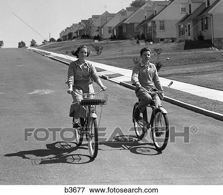 1950S Teen Boy Girl Couple Riding Bikes Down Residential Street View Large Photo Image Stock Photo - 1950S Teen Boy Girl Couple Riding Bikes Down Residential Street . Fotosearch