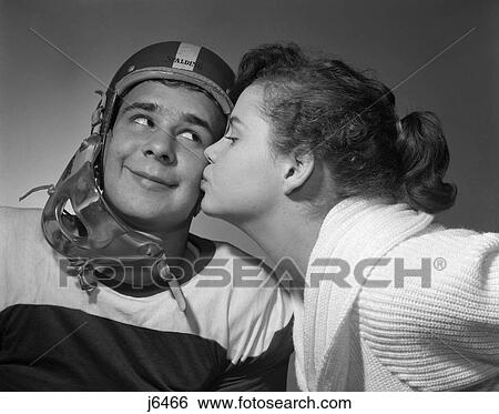 1950S Teen Girl Pony Tail Kissing Boy Wearing Football Helmet On The Cheek View Large Photo Image Stock Photograph - 1950S Teen Girl Pony Tail Kissing Boy Wearing Football Helmet On The Cheek . Fotosearch