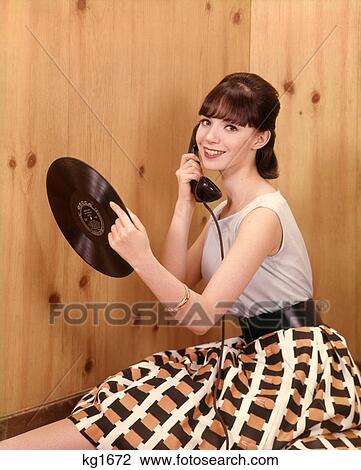 Stock Image - 1950S Teenage Girl Talking On Telephone And Holding Long Playing Lp Record Indoor Nostalgia Belt Skirt . Fotosearch