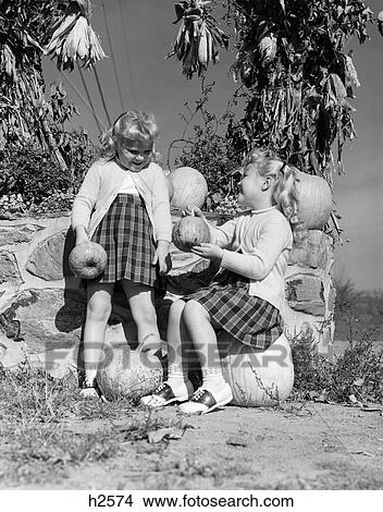 Picture - 1950S Twin Girls Sitting On Pumpkins Corn Husks Hanging To Dry Fall Harvest Outdoor . Fotosearch