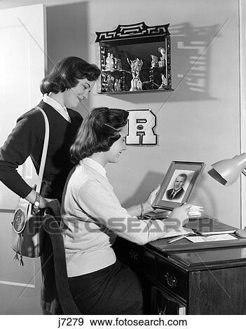 Stock Photo - 1950S Two Teen Girls Students One Seated At Desk Holds Up Framed Photo Of College Boyfriend . Fotosearch