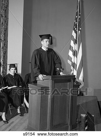 1950S Valedictorian Giving Speech At Podium With Other Graduates Seated In Background Holding Diplomas View Large Photo Image Picture - 1950S Valedictorian Giving Speech At Podium With Other Graduates Seated In Background Holding Diplomas . Fotosearch